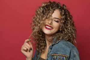 Woman with curly bronde balayaged hair against a red background